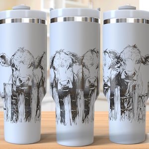 May include: Three white stainless steel tumblers with a black and white graphic of three cows looking over a fence. The tumblers have a silver lid and a handle.