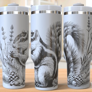 May include: Three stainless steel tumblers with a white background and black and white illustrations of a squirrel. The tumblers have a handle and a lid. The illustrations on the tumblers are different. One tumbler has a squirrel holding a nut, another has a squirrel sitting up, and the third has a squirrel with its tail curled up.