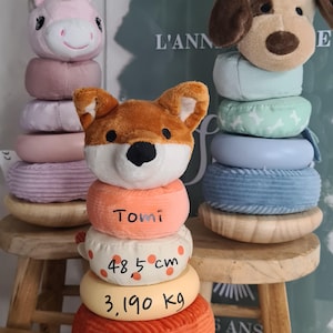 Peut inclure: Jeu d'empilage avec des têtes d'animaux, dont un renard, une licorne et un chien. Le jouet renard porte le nom "Tomi", avec des mesures de 48,5 cm et 3,190 kg. La date et l'heure sont inscrites sur l'anneau inférieur.