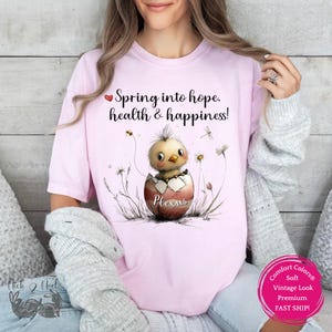 May include: Pink t-shirt with a cute cartoon chick hatching from an egg. The egg is decorated with the word "Plexus". The text on the shirt reads "Spring into hope, health & happiness!"