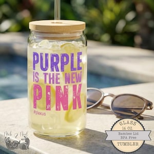 Puede incluir: Un vaso de vidrio transparente con tapa de bambú, lleno de un líquido amarillo y hielo. El texto "PURPLE IS THE NEW PINK" está impreso en la parte delantera. El vaso es de 473 ml y sin BPA. Gafas de sol descansan al lado.