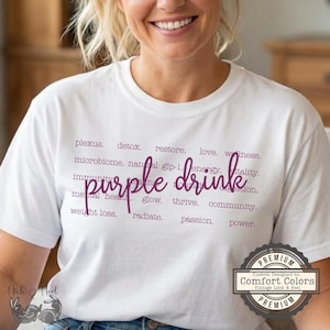 May include: A white t-shirt with the words "purple drink" in a cursive font, with related words in a smaller font. The shirt also has a "Comfort Colors" vintage-style logo.
