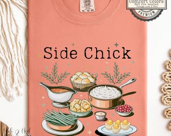 May include: A coral Comfort Colors t-shirt featuring the text "Side Chick" above illustrations of various side dishes. The design includes a gravy boat, mashed potatoes, green beans, and deviled eggs. The shirt has a vintage look.
