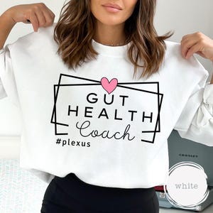 May include: White sweatshirt with a black graphic that says "Gut Health Coach" with a pink heart and the hashtag "#plexus".
