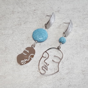 May include: A pair of silver earrings with blue lava rock beads and a silver face outline design.