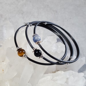 May include: Three black rubber bracelets with silver accents and gemstone beads. The beads are blue, brown, and black.