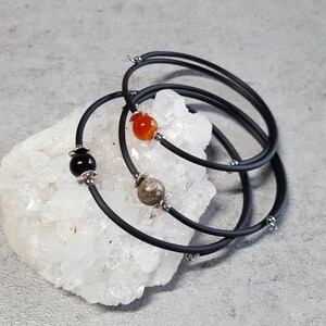 May include: Three black silicone bracelets with silver accents and gemstone beads. The bracelets are stacked on top of each other and feature a carnelian bead, a black onyx bead, and a brown jasper bead.