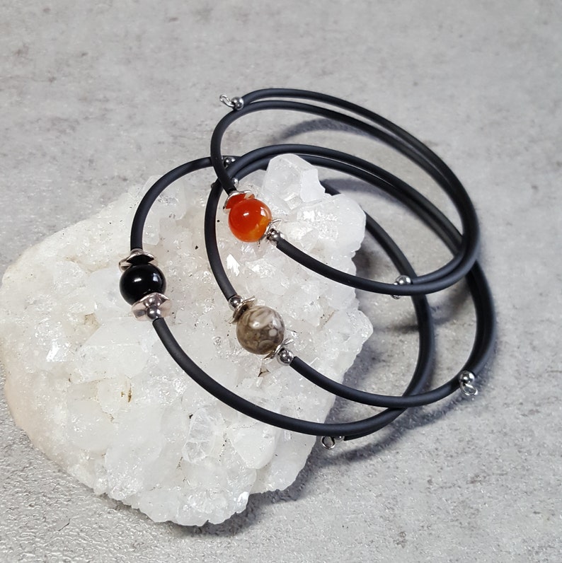May include: Three black silicone bracelets with silver accents and gemstone beads. The bracelets are stacked on top of each other and feature a carnelian bead, a black onyx bead, and a brown jasper bead.
