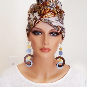 May include: A woman wearing a white and brown floral patterned turban with long, dangling earrings. The earrings are made of wood and feature blue and yellow circles.