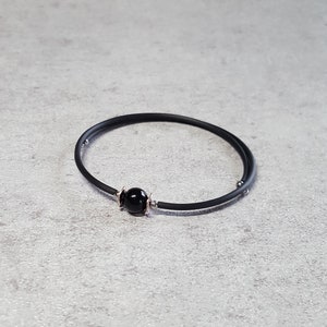 May include: A black rubber bracelet with a single black bead and silver accents.