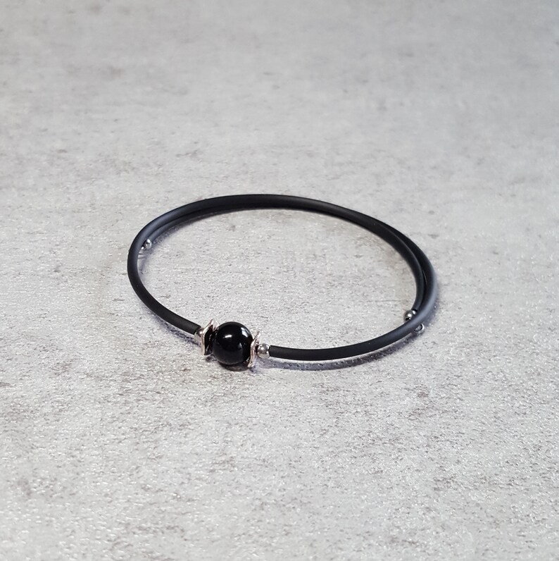 May include: A black rubber bracelet with a single black bead and silver accents.