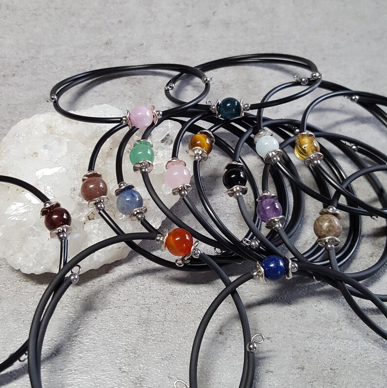 May include: A set of black elastic bracelets with different colored gemstone beads. The beads are round and smooth, and they are arranged in a random order. The bracelets are all the same size and are made of a stretchy material.