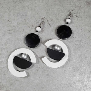 May include: A pair of geometric earrings with black and white wooden circles and silver beads. The earrings are suspended from silver hooks.