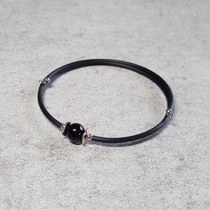 May include: A black rubber bracelet with a single black bead and silver accents.
