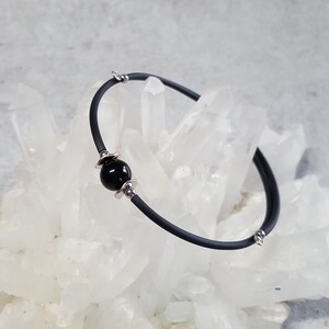 May include: A black elastic bracelet with a single black bead and silver accents.