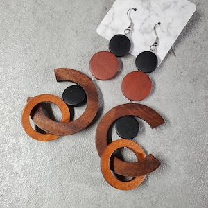 May include: A pair of wooden earrings with geometric shapes and black, brown, and red accents. The earrings are made of wood and have a unique design.