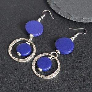 May include: A pair of dangle earrings with silver hoops and blue wooden circles. The hoops have a textured finish.