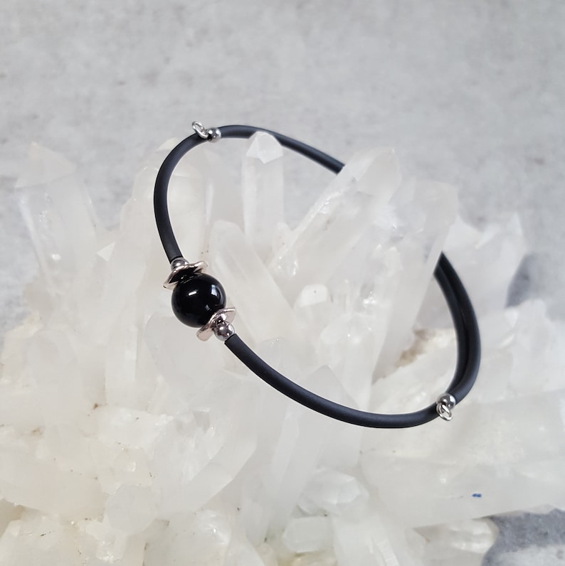 May include: A black rubber bracelet with a single black bead and silver accents.