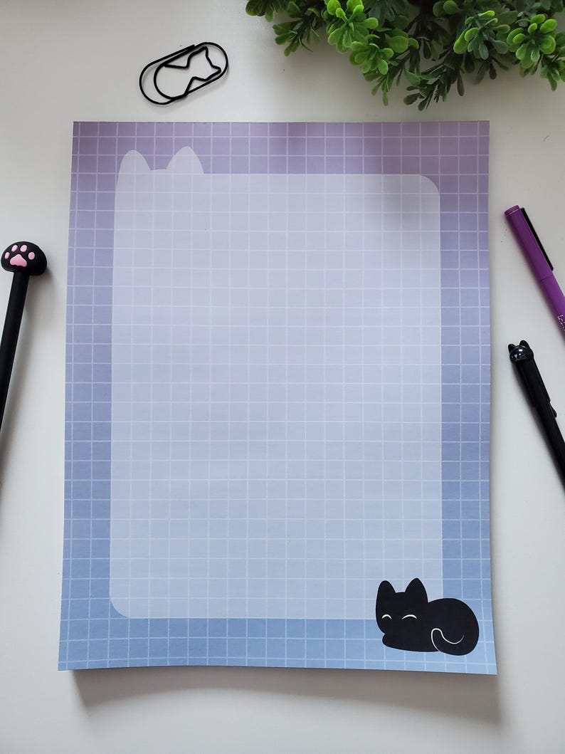 May include: A notepad with a blue and purple gradient background and a grid pattern. The top of the notepad has a cat ear design, and a black cat illustration is at the bottom. Pens with cat-themed designs are on the sides.