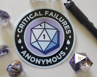 May include: A collection of polyhedral dice with a marbled white, purple, and gold design, scattered around a sticker. The sticker reads "Critical Failures Anonymous" with a D20 graphic. A black pen with a cat-shaped top is also present.