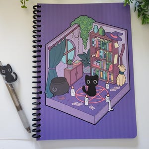 May include: A spiral-bound notebook with a purple cover featuring a cartoon illustration of a witch's room with a black cat, cauldron, and bookshelf. A black cat pen is next to the notebook.