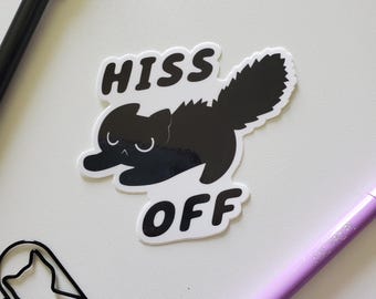 May include: A sticker with a black cartoon cat and the words "HISS OFF". The cat is in a defensive posture. A black cat-shaped paperclip and pens are also in the image.