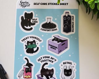 May include: A sticker sheet with a light blue background, featuring black cat illustrations and self-care themed phrases. Stickers include "Self Care," "Comfort Zone," and "Stay Hydrated." The sheet also has a "Retail Therapy" sticker.