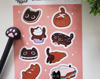 May include: A pink sticker sheet with cat-themed bakery items. The sheet includes stickers of a cupcake, croissant, and sandwich, all with cat features. The text "Smudge the Magic Cat" and "Bakery Sticker Sheet" are displayed on the sheet.