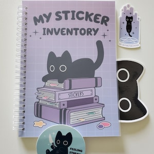 May include: A spiral-bound notebook with the text "MY STICKER INVENTORY" and a black cat illustration. Includes several stickers with cat designs and the phrases "CAT DISTRIBUTION SYSTEM" and "FEELING STABBY". A black cat-shaped paperclip is also present.