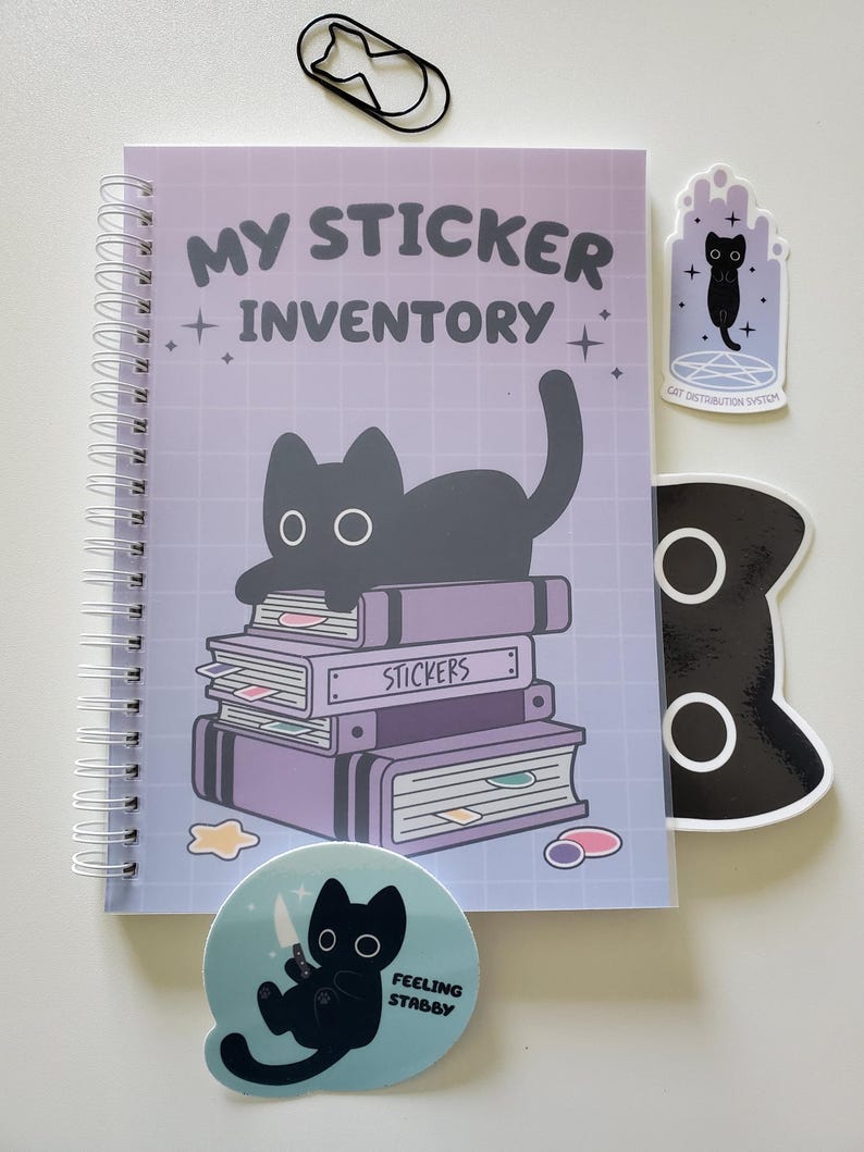 May include: A spiral-bound notebook with the text "MY STICKER INVENTORY" and a black cat illustration. Includes several stickers with cat designs and the phrases "CAT DISTRIBUTION SYSTEM" and "FEELING STABBY". A black cat-shaped paperclip is also present.