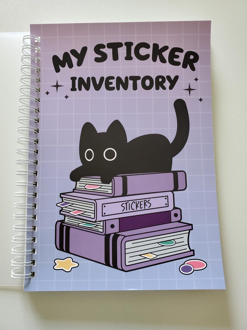 May include: A spiral-bound notebook with a purple cover featuring the text "MY STICKER INVENTORY" and a black cat illustration. The cat is perched atop a stack of purple books labeled "STICKERS". The background has a grid pattern.