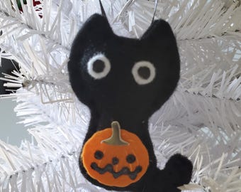 May include: Black cat decoration with white eyes and an orange pumpkin. The cat is made of felt and has a black ribbon for hanging. The pumpkin has a carved face. A Halloween decoration.