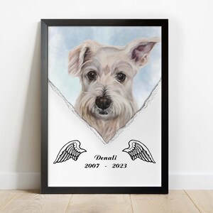 Könnte beinhalten: Ein schwarzer gerahmter Druck mit weißem Hintergrund und einem zerrissenen Rand. Ein weißer Hund mit schwarzen Augen und einer rosa Nase schaut durch den zerrissenen Rand. Der Name des Hundes, "Denali", und die Daten "2007 - 2023" sind unter dem Hund gedruckt. Zwei schwarze Engelsflügel befinden sich auf beiden Seiten des Textes.
