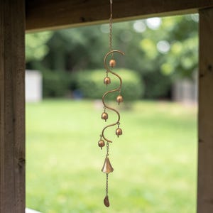 May include: A decorative wind chime with a series of small, bronze-colored bells suspended from a curved metal frame. The bells are of varying sizes and shapes, creating a visually appealing and melodic design. The chime hangs from a chain, adding to its overall aesthetic.