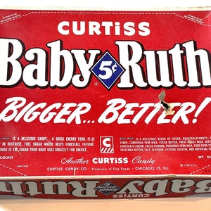 May include: A red and white box for Baby Ruth candy bars. The box has the words "CURTISS Baby Ruth 5¢ BIGGER BETTER!" printed on it. The box also has a blue diamond with the number 5 in it. The box is made of cardboard and has a white background with red lettering. The box is 2 1/2 pounds.