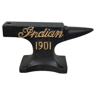 May include: A black cast iron anvil with the word "Indian" in gold script and the number "1901" in gold block letters. The anvil has a rectangular base, a central body, and a pointed horn.