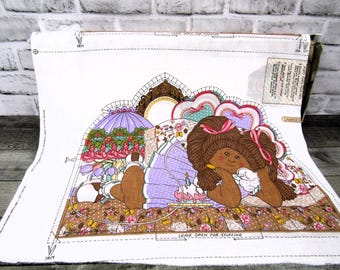 May include: A fabric panel featuring a brown-skinned girl with brown hair, wearing a purple dress and holding a white bird. She is lying on a bed with a floral pattern. The panel is bordered in white with sewing instructions. The text on the panel reads "Leave open for stuffing."