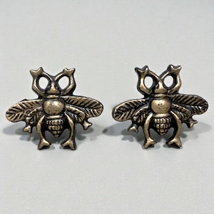 May include: Two bronze-colored bee-shaped cabinet knobs. Each knob features detailed wings, a segmented body, and antennae. The knobs are designed with a vintage aesthetic, suitable for furniture or decorative projects.