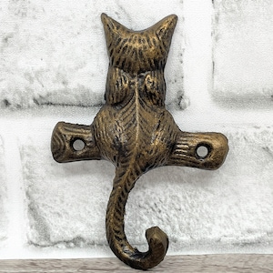 May include: A gold-toned metal cat hook with a detailed design. The cat is sitting on a branch with its tail curled around the hook.
