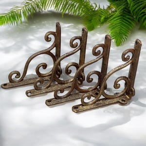 May include: Four ornate metal shelf brackets with a scrolled design. The brackets are a dark gold color and have a distressed finish.