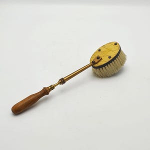 以下が含まれることがあります： 木製の柄と真鍮製のステムが付いたアンティークブラシ。楕円形のブラシヘッドには明るい色の毛があり、真鍮のリベットで固定されています。ハンドルは濃い茶色です。