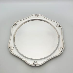 Peut inclure: Un plateau de service argenté poli avec un centre circulaire lisse et un bord festonné. Le rebord présente une bordure surélevée avec des accents décoratifs en forme de feuille à chacun des six points le long du périmètre du plateau en métal.
