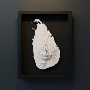 以下が含まれることがあります： 黒い背景に、スリランカの立体的な白いレリーフ地図が額装されています。 地図は黒いフレームに収められ、島の地形が示されています。 アートワークは濃い灰色の壁に設置されています。