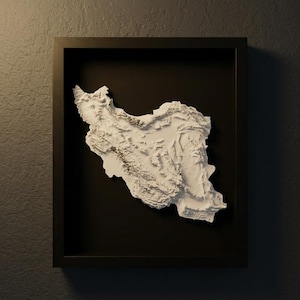 Op de afbeelding: Een ingelijste, driedimensionale reliëfkaart van Iran. De witte kaart staat tegen een zwarte achtergrond in een zwart frame. Het reliëf toont de topografie van het land met gedetailleerde texturen en schaduwen.