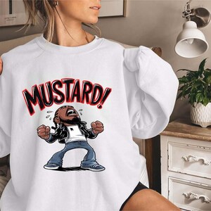 May include: White sweatshirt with a cartoon illustration of a person with a distressed expression. The text "MUSTARD!" is above the illustration.