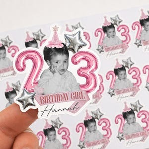 May include: Sheet of stickers featuring a child's photo, pink number balloons, and star accents. The stickers say "Birthday Girl Hannah" and the number "23". The stickers are designed for a birthday celebration.