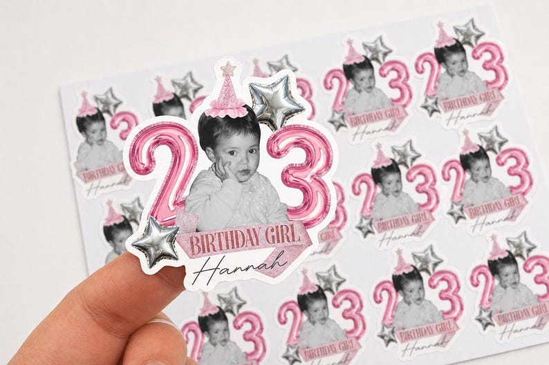 May include: Sheet of stickers featuring a child's photo, pink number balloons, and star accents. The stickers say "Birthday Girl Hannah" and the number "23". The stickers are designed for a birthday celebration.