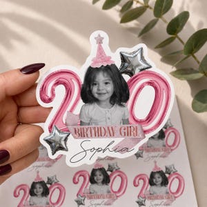 May include: A sheet of stickers featuring a young girl's photo, a pink '20' balloon design, and the text 'BIRTHDAY GIRL Sophia'. The stickers include silver star accents and a pink party hat.