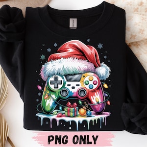 May include: A black sweatshirt featuring a colorful video game controller wearing a red Santa hat. The design includes a string of Christmas lights, a small gift box, ornaments, and snowflakes. The text PNG ONLY is printed at the bottom.