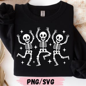 May include: A black long-sleeve sweatshirt featuring a white graphic print of three dancing skeletons surrounded by small four-pointed stars. The text PNG/SVG is printed in black at the bottom center of the image on a light pink background.